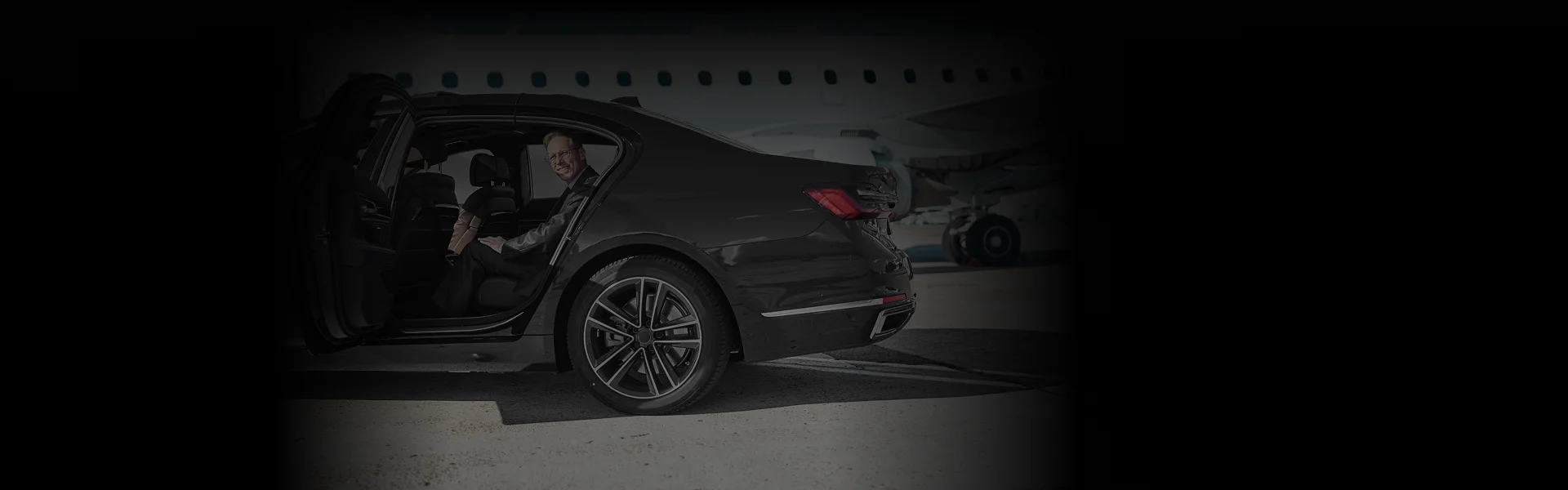 Black luxury sedan in side rear angle with passenger seated and smiling, promoting Dulles Airport Car Service with sleek UI overlay for booking.